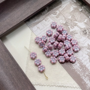 Macro detail of pink glass flower beads with blue edges and golden craft pins