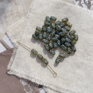 Macro view of olive green Czech glass beads with white X pattern on rustic linen