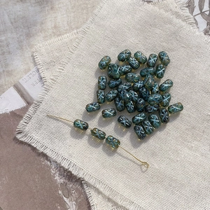 Macro view of dark green glass beads with light blue X-pattern for DIY jewelry