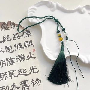 Detailed view of dark green silk tassel with white jade bead on white ceramic tray
