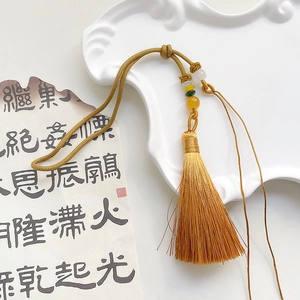 Close-up of golden silk tassel with decorative beads on a vintage calligraphy background