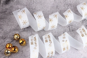 Dettaglio di nastro grosgrain bianco con scritta Merry Christmas dorata e fiocchi