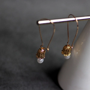Close-up of 18K gold lily of the valley earrings with white pearl pendants on stand