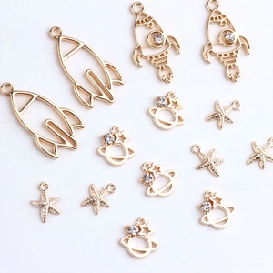 Detail of DIY jewelry charms including golden rocket, crystal planet, and starfish pendant