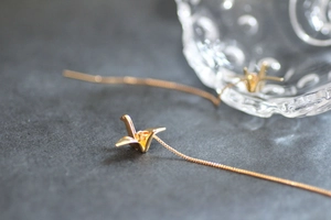 Vue macro de boucles d'oreilles traversantes grue origami dorées à l'or fin 14 carats