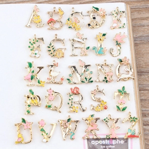 Detail of 26 enamel alphabet charms with floral and animal motifs on a wood table
