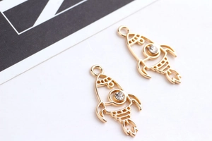 Macro detail of golden rocket-shaped alloy charms with white rhinestones for DIY jewelry