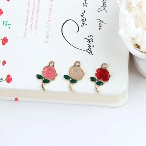 Dettaglio di tre ciondoli a forma di rosa in smalto rosa, beige e rosso con foglie verdi