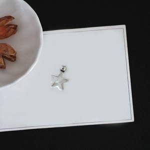 Macro detail of a silver star-shaped hollow charm for DIY earring making on a white plate