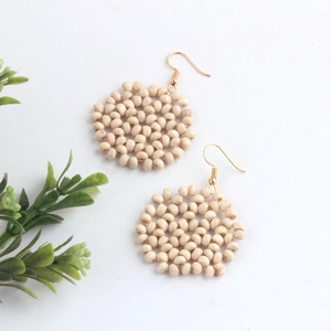 Close-up of bohemian round drop earrings with woven cream wooden beads and gold hooks