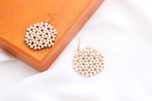 Close-up of Bohemian cream beaded round drop earrings with gold metal hooks on silk