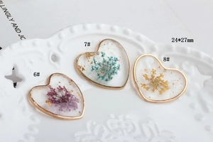 Close-up of three heart-shaped resin pendants with colorful dried flowers and gold foil