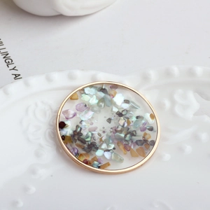 Detail of round gold pendant with rainbow shell flakes and resin inlay on ceramic plate