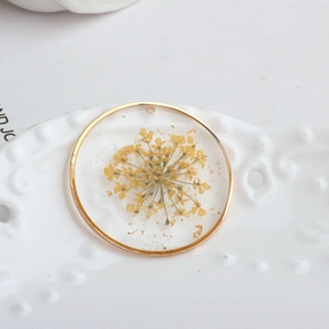 Macro detail of handmade resin pendant featuring yellow dried flower and gold foil flakes