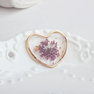 Close-up of heart-shaped resin pendant with purple dried flowers and gold foil