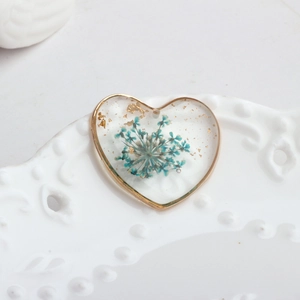 Close-up of heart resin pendant with blue dried flowers and gold foil accents