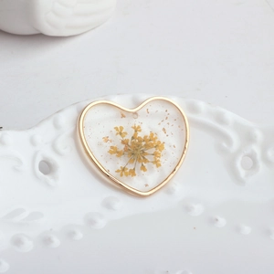 Detail of heart-shaped resin pendant with yellow dried flower and gold foil on ceramic tray