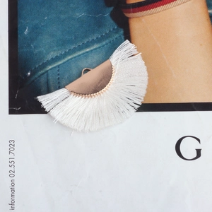 Macro detail of a white fan-shaped cotton tassel pendant with rose gold metal fastener