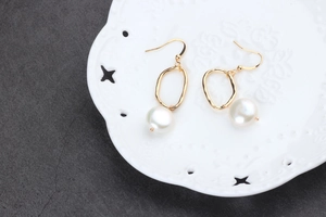Detailed macro view of baroque pearl drop earring with brushed gold irregular metal oval