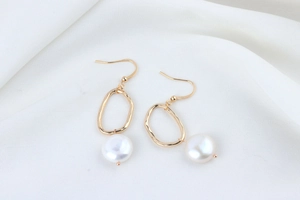 Detail of gold branch style earrings with white flat pearl drops on white fabric