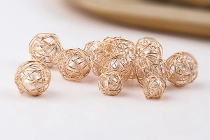 Detalle de esferas doradas envueltas en alambre con perlas blancas para crear joyería