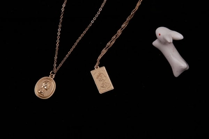Detailed view of rose gold Elizabeth II portrait embossed necklaces on black background