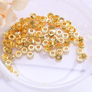 Macro view of 14K gold plated spacer beads with textured wheel design in a clear box