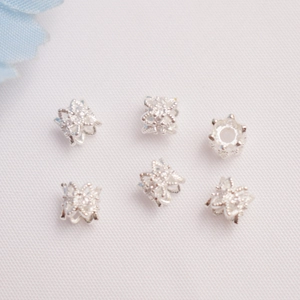 Dettaglio macro di sei perline distanziatrici a fiore cavo argento per gioielli DIY