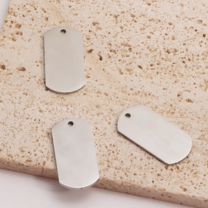 Brushed stainless steel military dog tag pendants displayed on a beige stone surface