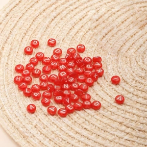 Flat round red acrylic letter beads for DIY jewelry on a woven straw mat background
