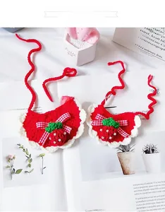 Detail of handmade knit strawberry pet bib with white lace edge and gingham bow tie