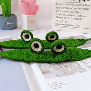 Detail of green knitted frog headbands for pets with 3D eyes on a white magazine background
