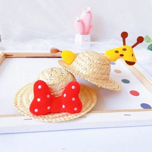 Detail view of mini pet straw hats with red polka dot bow and yellow giraffe designs
