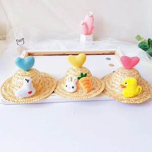 Close-up of three mini hand-woven pet straw hats featuring cute plush hearts and cartoon toys