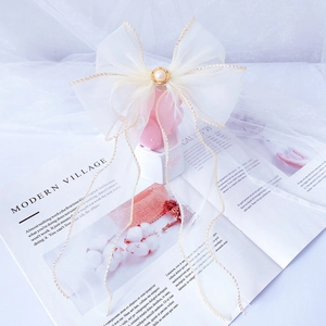 Detailed view of white organza bow hair clip with gold edges and long elegant ribbons