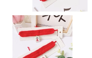 Close-up of a red crochet pet collar with a Mahjong tile pendant on a display card