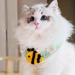 Close-up of hand-knitted pet collar with bee and daisy decorations on a fluffy cat