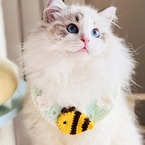 Detail of hand-knitted pet collar featuring a crochet bee charm and green-white flower pattern