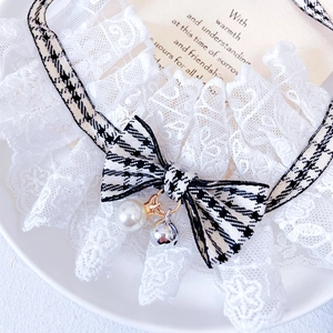 Detailed view of white lace pet collar with houndstooth bow and pearl bell accessory