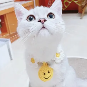 Handmade knitted pet collar with yellow smiley face and white flower on a white cat