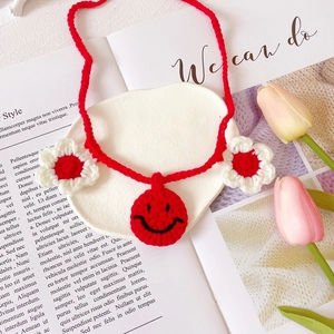 Detail of red crochet pet collar featuring a happy face charm and white knit flowers