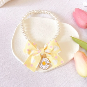 Detail view of pearl pet necklace with yellow bow and daisy charm on display