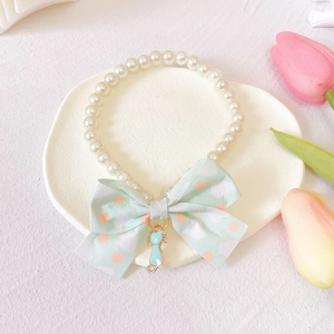 Close-up of pearl pet necklace with green polka dot bow and blue cat pendant