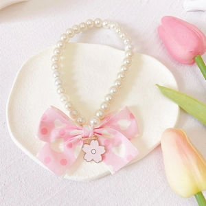 Detail of pet necklace featuring pearls, pink bow with hearts and flower pendant