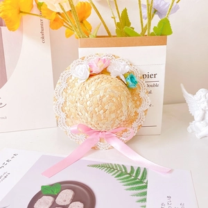Detail of woven straw pet hat featuring lace trim, floral accents and a pink satin bow