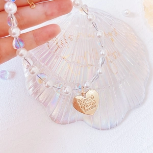 Macro shot of pearl pet necklace featuring a gold heart charm with engraved text detail