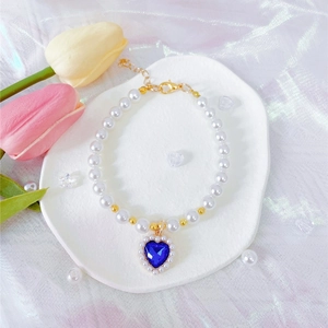 Macro view of blue heart sapphire charm on pearl pet necklace with golden lobster clasp