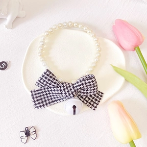Detail of white pearl pet necklace with a houndstooth bow and bell in a decorative tray