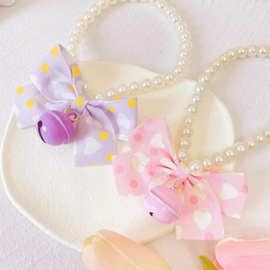 Detail of pink and purple pet pearl necklaces with bowknots and bells on a white tray