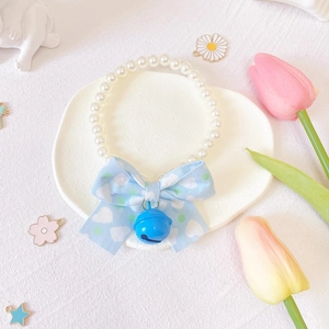 Close-up of pearl pet collar with blue heart bow and bell in a heart-shaped tray